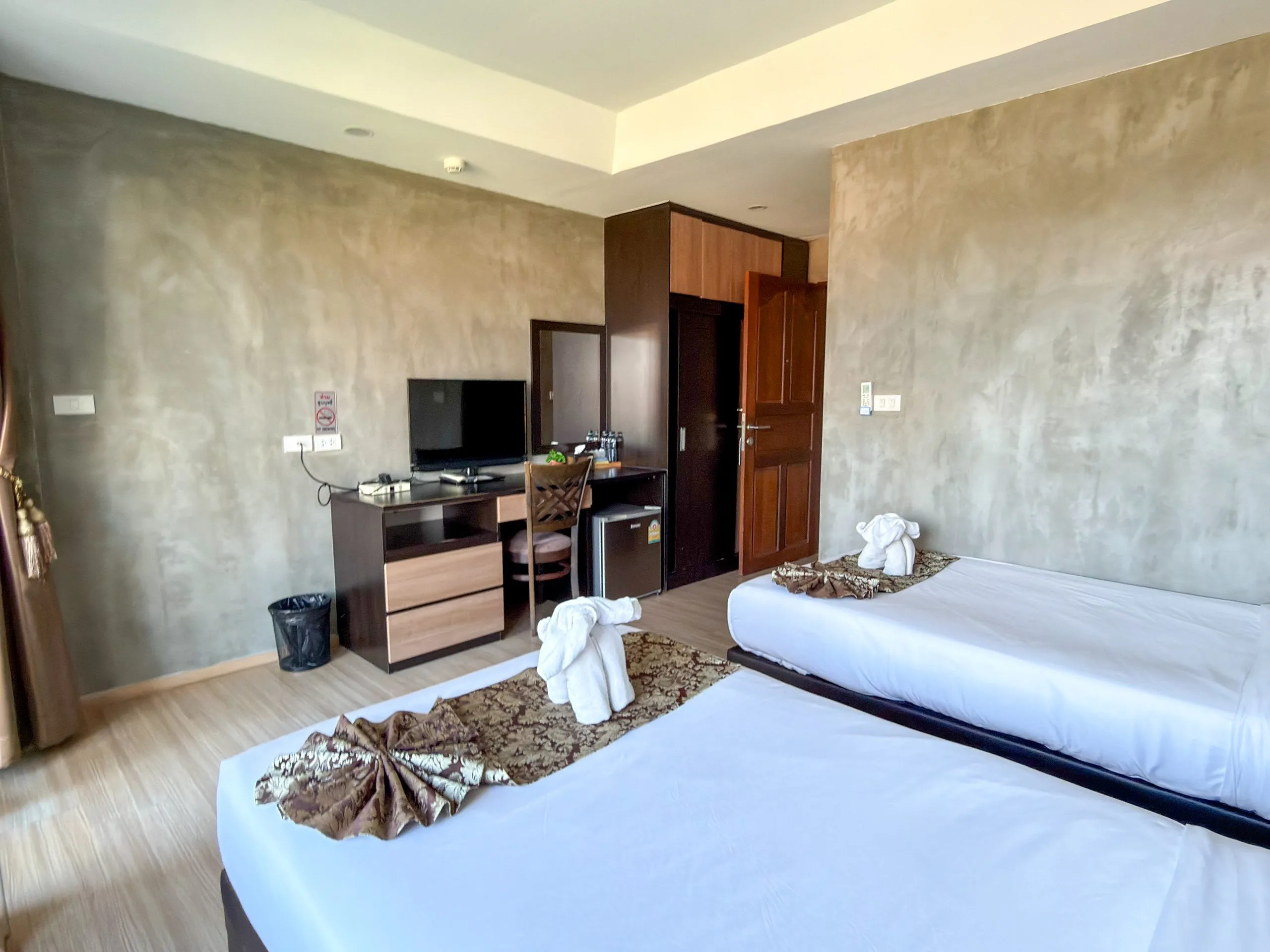 Standard Twin room: work desk with TV and mini fridge, single bed with a towel elephant in front