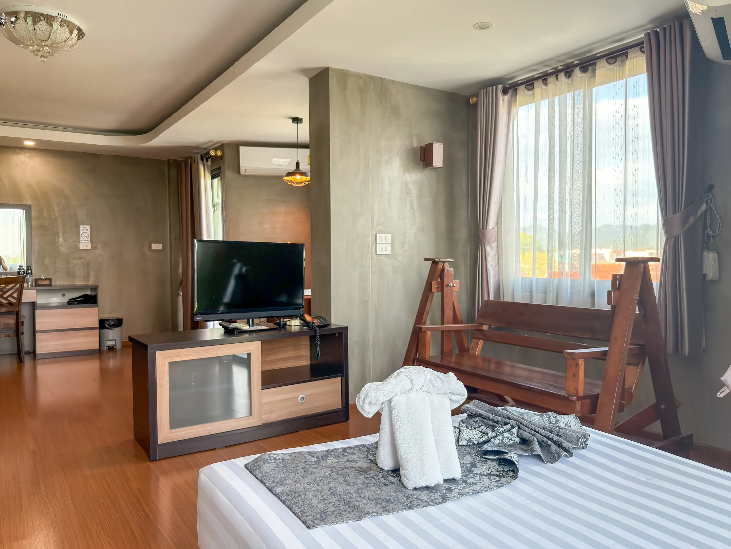 Studio: TV on a cabinet and a wooden bench seat by the window, towel elephant on the bed