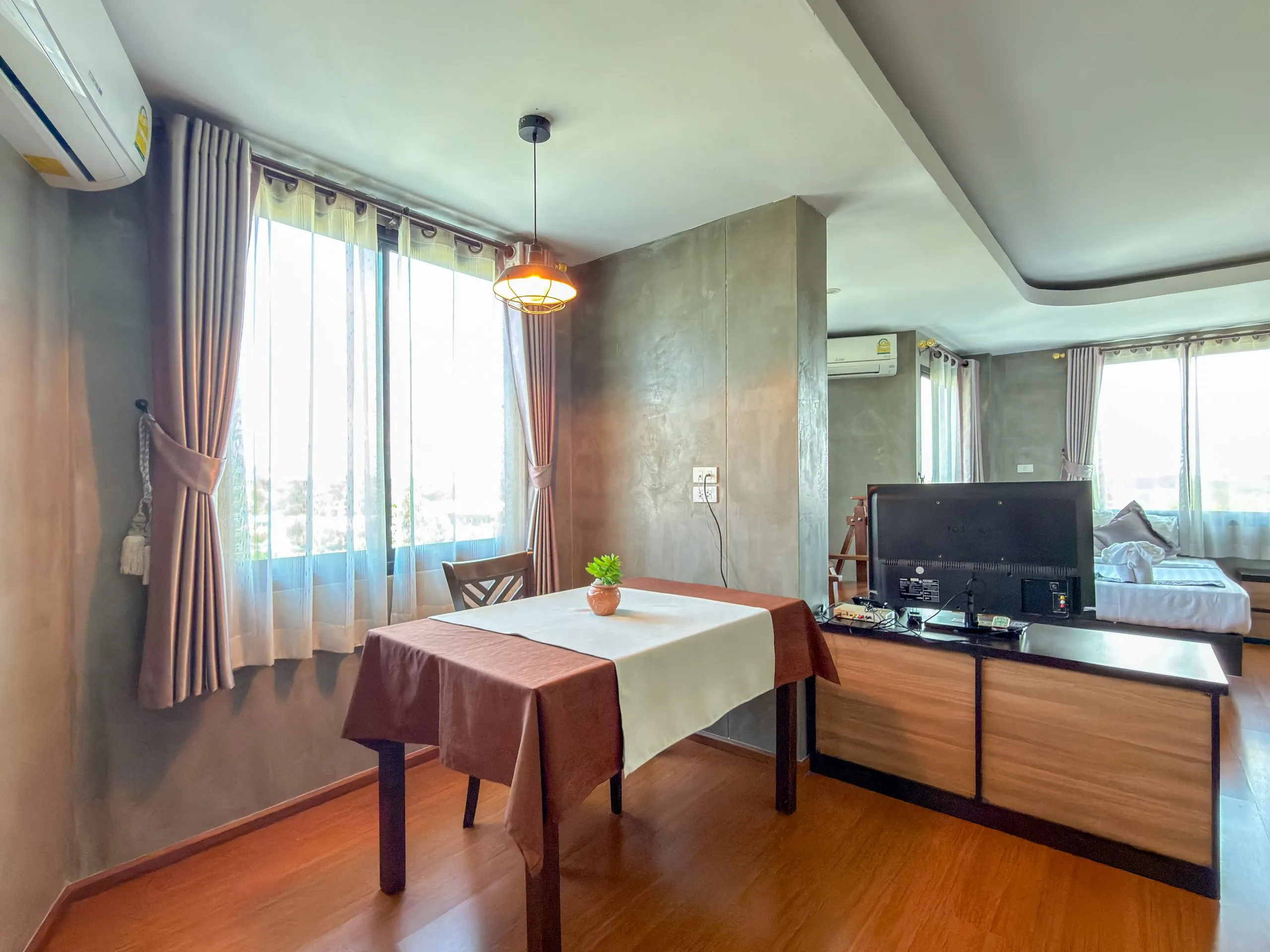 Studio: dining table by the window, TV cabinet and a bed beyond
