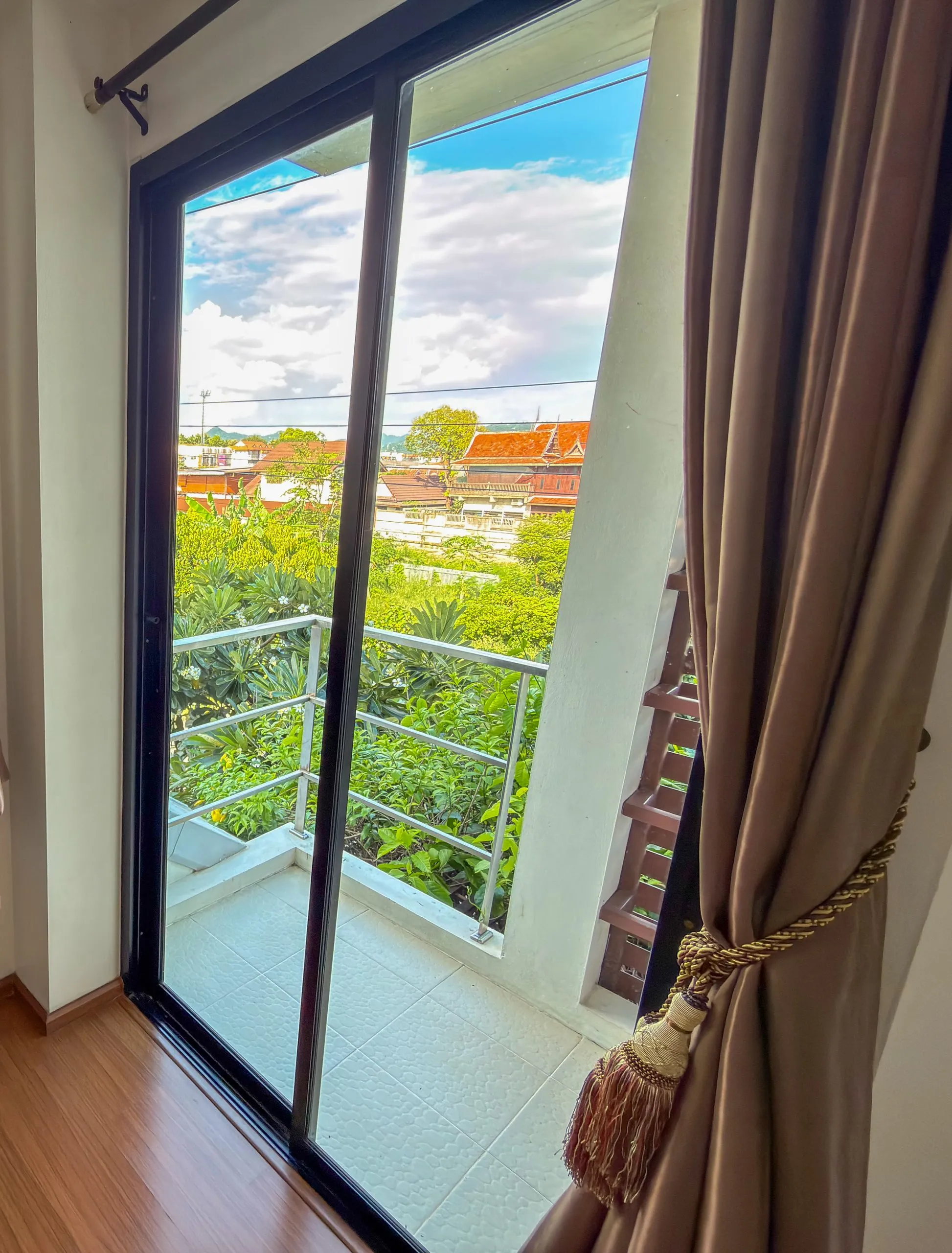 View from the Superior King balcony door: trees and rooftops, curtain with tassel