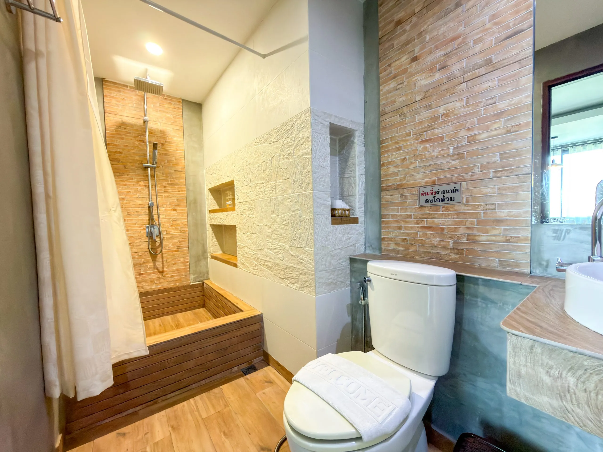 Studio bathroom: toilet, brick-effect tile wall and a shower behind a curtain